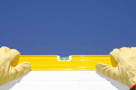 Hands of construction worker with gloves on spirit or water level tool outdoor, with blue sky as background and copy space.の写真素材