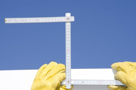 Hands of construction worker with gloves and ruler isolated on blue sky as background and copy...