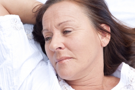 Portrait attractive mature woman resting in bed with sad and contemplating expression.の写真素材