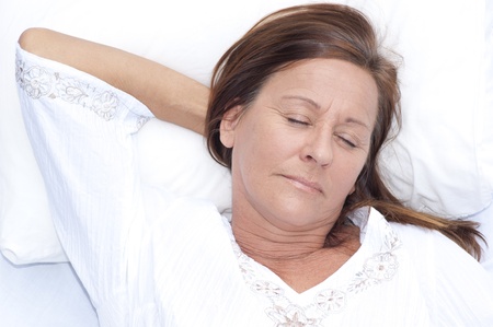 Portrait relaxed attractive mature woman asleep, resting in bed with closed eyes and smile on face, peaceful, happy expression, enjoying leisure lifestyle.の写真素材