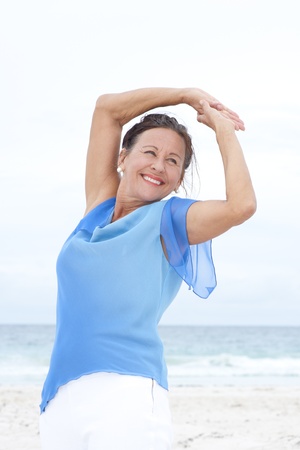 Portrait Beautiful mature woman confident and happy at beach, wearing blue blouse, with ocean and white overcast sky as blurred background and copy space.の写真素材