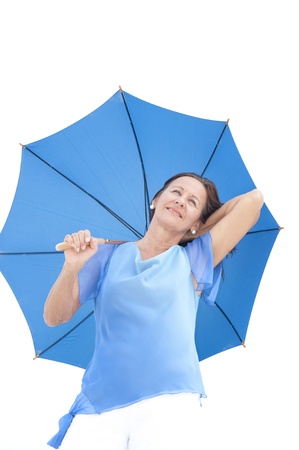 Portrait attractive mature woman standing happy and relaxed with closed eyes and blue umbrella, isolated with bright white sky as blurred background and copy space.の写真素材