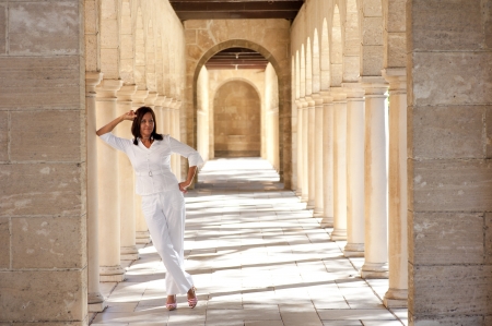 Portrait confident attractive mature woman standing dressed in white and high heel shoes in historic stone archway at sunny day, with blurred background and copy space.の写真素材