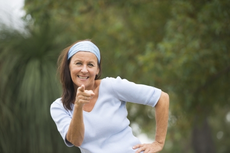 Portrait attractive mature woman, happy and confident, with finger pointing, wearing blue shirt and headband, outdoor and blurred background.の写真素材