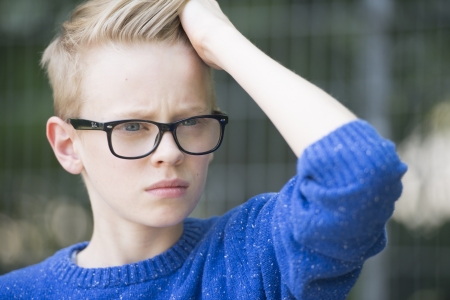 Portrait confident blond teenage boy wearing glasses with serious face, blurred background.の写真素材