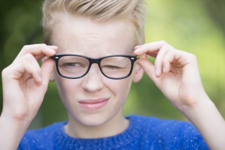 Portrait smart looking blond teenager with glasses and a blink of an eye, thoughtful and cleverの写真素材
