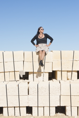 Portrait sexy mature woman with, wearing skirt, fishnet stockings and boots, is sitting confident, relaxed on wall, isolated with clear blue sky as background and copy space.の写真素材