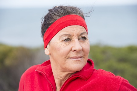 Portrait attractive middle aged woman, happy, relaxed, sporty, friendly, positive, successful, enjoying active retirement outdoor, wearing red sweater and headband, with blurred background.の写真素材