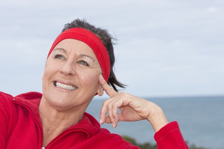 Portrait beautiful mature woman, happy, relaxed, sporty, friendly, positive, successful, enjoying active retirement outdoor, wearing red sweater and headband, with blurred background.の写真素材