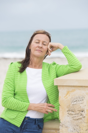 Portrait attractive mature woman standing relaxed and happy confident with closed eyes outdoor, with ocean as blurred backgroundの写真素材