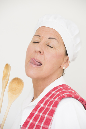 Portrait confident happy and attractive female cook in white chef workwear posing with tclosed eyes and tongue out, isolated on white の写真素材