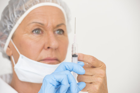 Portrait serious professional female hospital nurse in blurred background with syringe in hand with blue glove, isolated on white and copy space の写真素材