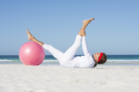 Relaxed attractive senior woman stretching exercise with gymnastic ball at beach.の写真素材