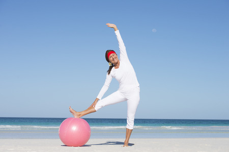 Fit and healthy attractive mature woman happy exercising with gymnastic ball at beach.の写真素材