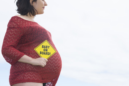 Close up of pregnant woman holding 'baby on board' sign at belly, blurred background and copy space.