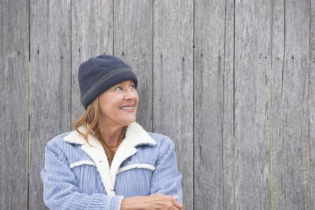 Portrait happy confident attractive mature woman outdoor, wearing warm bonnet and wool jacket, timber wall background, copy space.の写真素材
