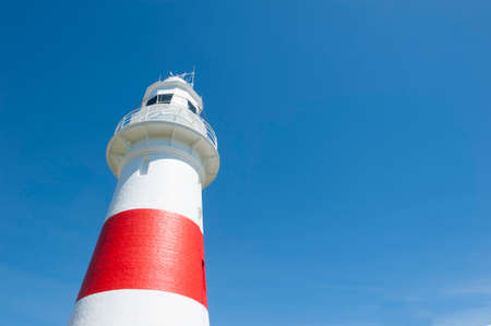 Top of Red white colored lighthouse at ocean coast, upward view, blue sky as background and copy space.の写真素材