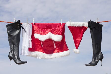 Female Santa Claus costume hanging on clothes line after washing, next to black high heel stiletto boots and white nylon stockingsの写真素材