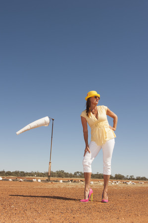 Portrait beautiful mature traveling woman standing alone on remote airfield of rural airport in outback Australia, posing in high heel shoes, with blue sky as background and copy space.の写真素材
