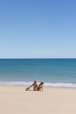 Portrait attractive senior woman sitting happy and relaxed with pet dogs at beach, with ocean and blue sky as background and copy space.の写真素材