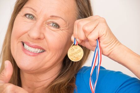 Close Up Portrait proud active attractive mature woman presenting confident happy smiling and positive thumb up her winning gold medal award.の写真素材