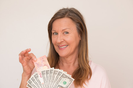Portrait attractive mature woman holding Euro and US dollar currency, isolated, bright background.の写真素材