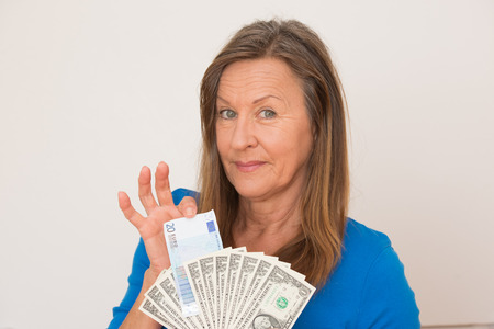 Portrait happy attractive mature woman presenting Euro and US dollar money, isolated, bright background.の写真素材