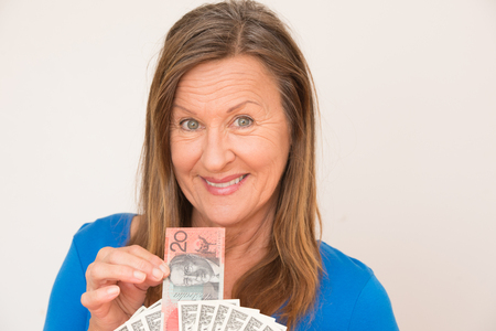 Portrait attractive mature woman holding relaxed smiling Australian and US dollar notes, isolated, bright background.の写真素材
