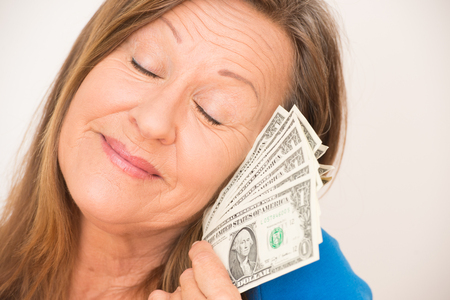Portrait attractive mature woman holding happy relaxed with closed eyes us dollar notes, isolated, bright background.の写真素材