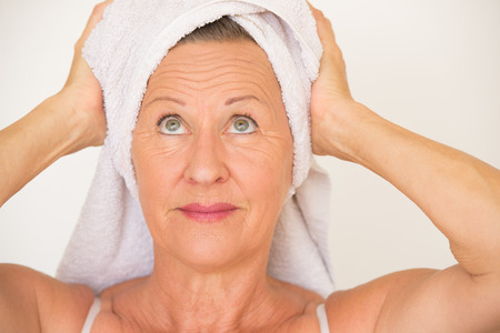 Portrait happy smiling healthy attractive mature woman with white spa towel on head, bright background.の写真素材
