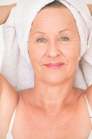 Portrait happy healthy attractive senior woman with white spa towel on head, bright background.の写真素材