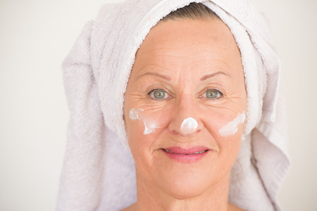 Portrait beautiful mature woman with towel and protective skin care creme and moisturiser lotion on...