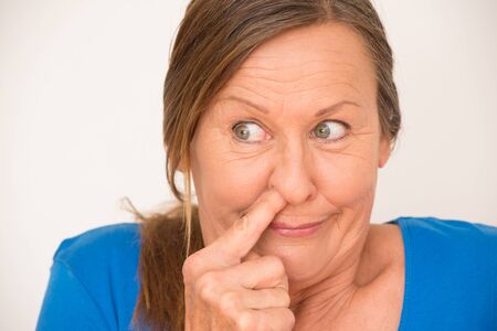 Portrait attractive mature woman making happy face, poking finger in nose, funny look, isolated, bright background.の写真素材