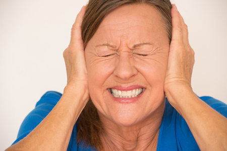 Portrait attractive mature woman in pain with migraine headache, covering ears with hands, closed eyes, isolated, bright background.の写真素材