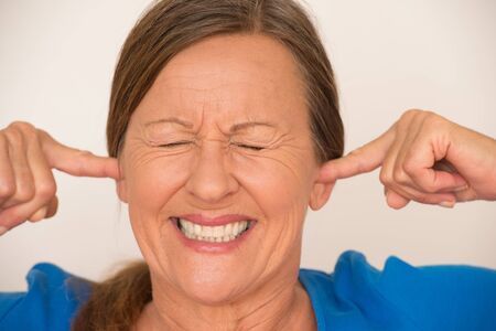 Portrait attractive mature woman covering noise from ears with finger, stressed facial expression, closed eyes, isolated, bright background.の写真素材