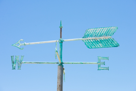 Patina green rusty old weather vane isolated on summer sunny blue sky background, with arrow and...