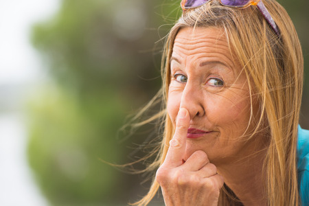 Portrait attractive mature woman with funny happy friendly relaxed smile, poking nose with finger, blurred background, outdoor copy space.の写真素材