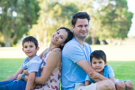 Portrait happy interracial hispanic caucasian family, relaxed together in park outdoors, blurred background.の写真素材
