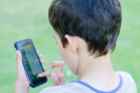 Back Portrait  young boy playing alone on smartphone in blurred background, internet and social media addiction concept.の写真素材