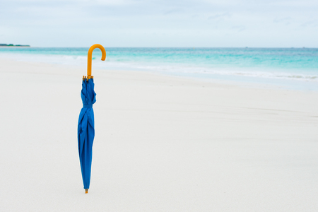 Blue umbrella in clean sand on remote beach at rainy storm day, blurred background with horizon, overcast sky, coastline, ocean and copy space.の写真素材