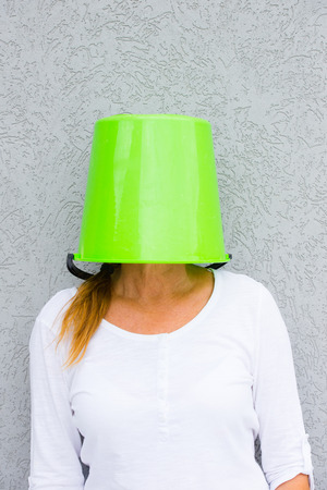 Portrait frustrated mature woman with bucket over head posing, isolated against grey wall outdoor.の写真素材