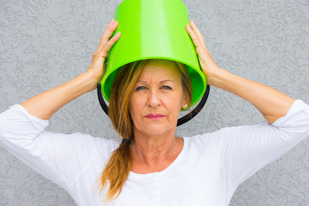 Portrait annoyed angry mature woman with bucket on head and posing, isolated against grey wall outdoor.の写真素材