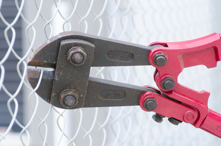 Close up detail of heavy metal bolt clipper with red handles cutting fence, blurred background and copy space.の写真素材