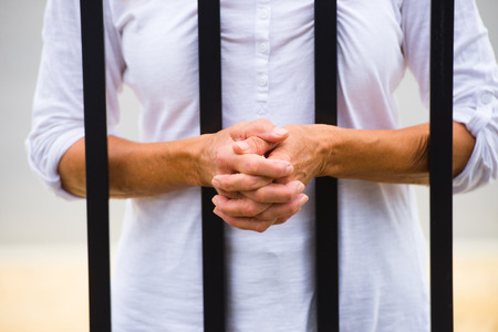 Close up Woman with hands behind metal bars in prison cell or cage, blurred background and copy space.の写真素材