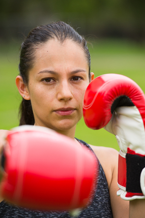 Portrait young confident attractive hispanic woman with boxing gloves training outside in park, blurred background.の写真素材