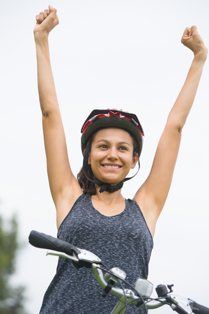 Portrait sporty successful attractive young hispanic woman on bicycle, arms up, joyful happy winning smile, isolated on white outdoor.の写真素材