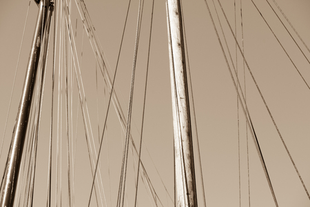 Sepia filtered image Mast of historic wooden sailing ship, with rigging and ropes, sunny blue sky as background and copy space.の写真素材