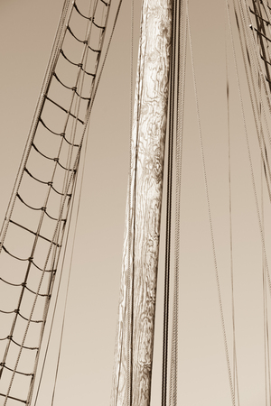 Sepia filtered image Mast of historic wooden sailing ship, with rigging and ropes, summer sunny blue...