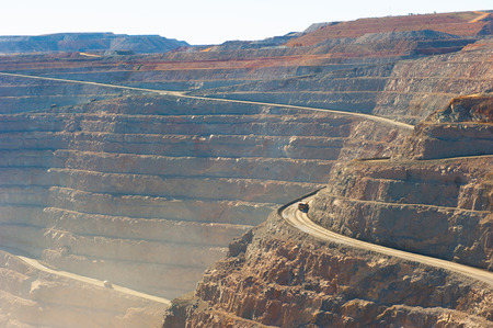 Panoramic aerial view of Super Pit goldmine in Kalgoorlie, Western Australia, with trucks on winding path along edges of the whole, heavy machinery, summer sunny dusty blue sky.の写真素材