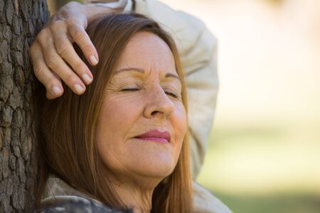 Portrait attractive mature woman relaxed in park with closed eyes, peaceful daydreaming, contemplating, thoughtful, blurred background.の写真素材